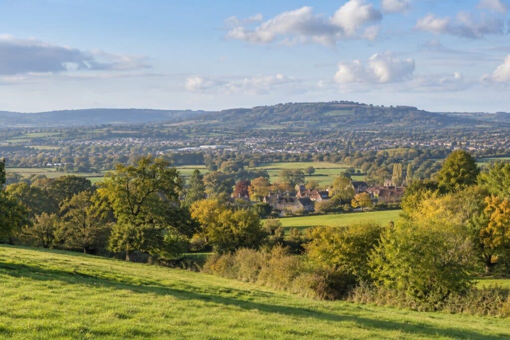 Gloucestershire local plan landscape with traditional village rooftops, green fields and wooded hills in the autumn countryside